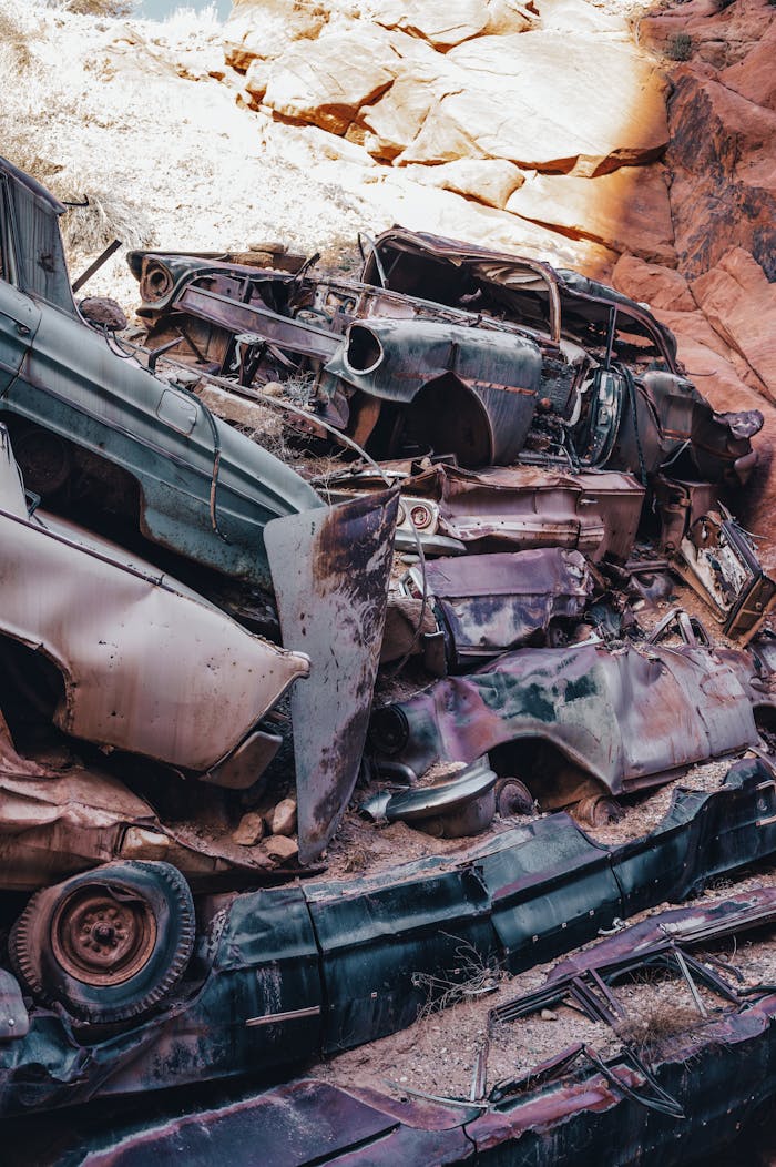 A vertical shot of rusty, stacked cars in an outdoor junkyard, surrounded by rocky desert terrain.