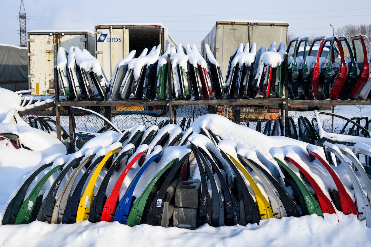 Colorful, snow-covered car doors stacked in an Estonian scrapyard during winter.