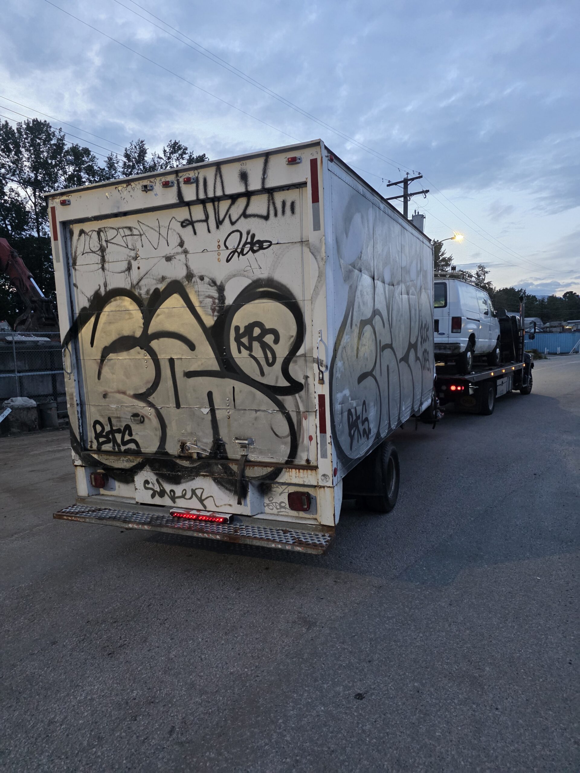 Graffiti-covered cube van box truck loaded on a flatbed for scrap in Coquitlam